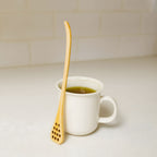 Bamboo honey dipper next to cup of tea