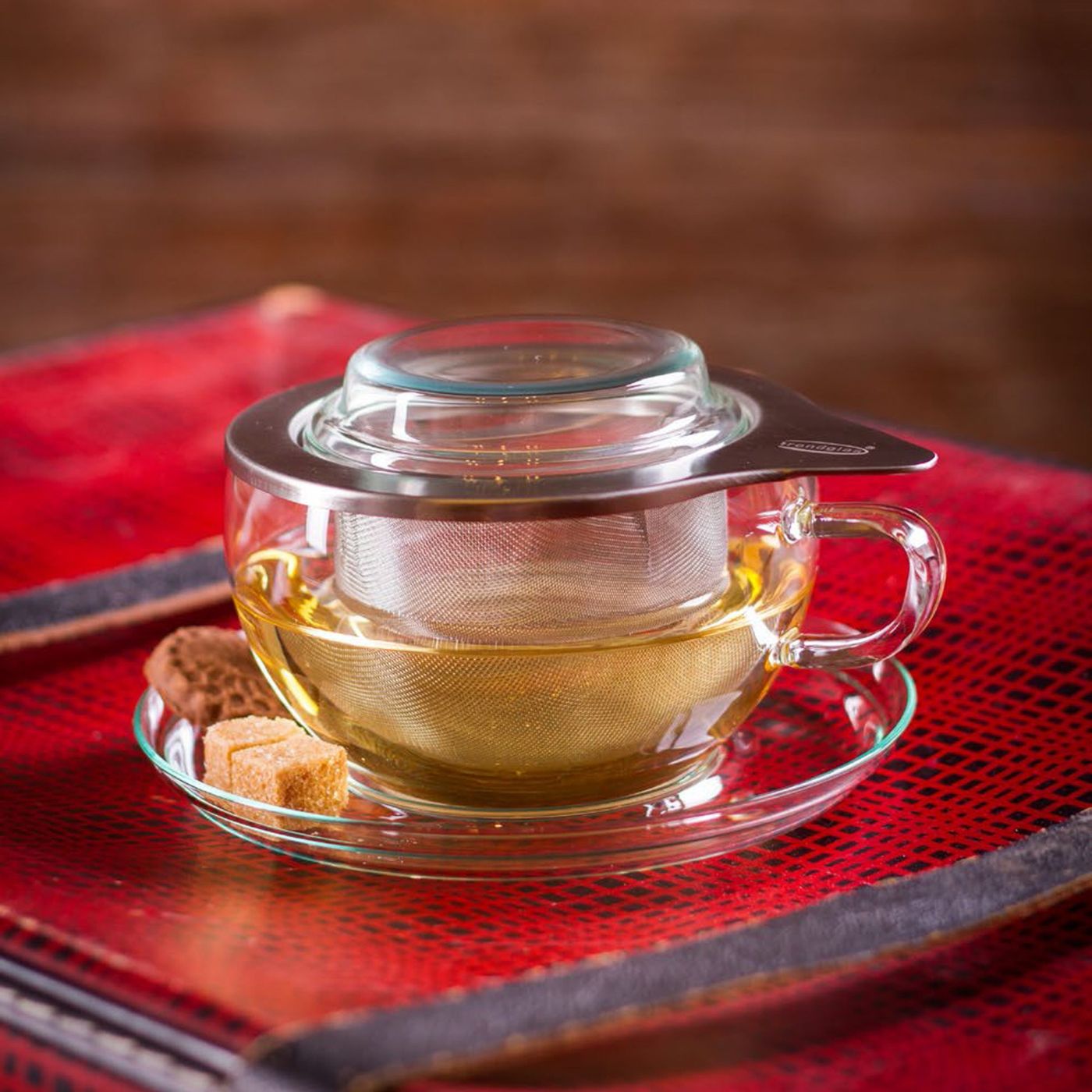 Loose leaf tea steeping in glass cup with steel strainer with cookies and sugar